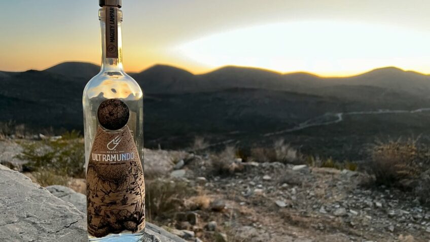 A bottle of Ultramundo with the backdrop of a sunset of the landscape